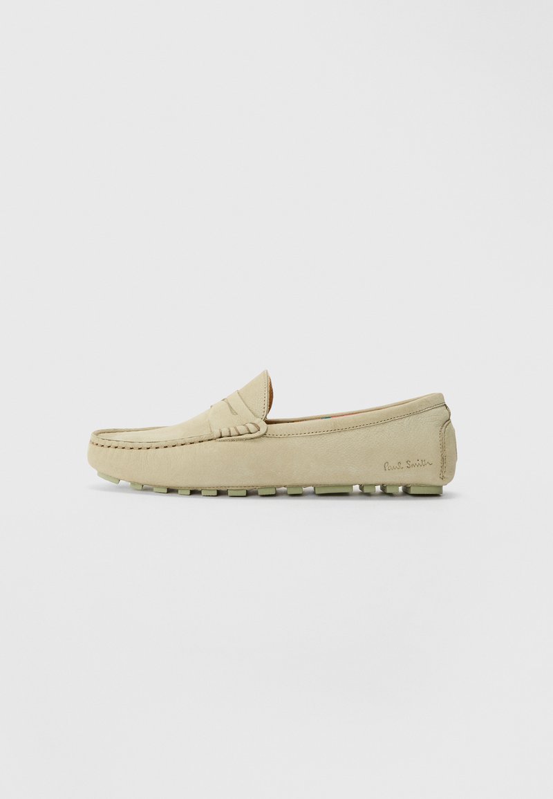 Mocassin léger beige, en daim, avec des accents cousus sur le bout, une semelle en caoutchouc texturée avec de petites bosses, et un logo de marque embossé sur le côté.