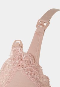 Spallina di reggiseno rosa morbida con fibbia regolabile in plastica e dettagli in pizzo floreale lungo il bordo su uno sfondo semplice.