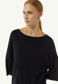 Schwarzes, locker sitzendes Oberteil mit weitem Ausschnitt und Fledermausärmeln aus weichem Material. Verfügt über subtile Nähte entlang der Seitennähte.