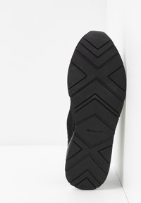 Black athletic shoe with a textured rubber sole, featuring a zigzag tread pattern and the brand name "GANT" embossed on the bottom.