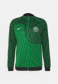 Chaqueta verde con cremallera hecha de un tejido texturizado que presenta un patrón triangular en tonos variados de verde y negro, con un logo en el pecho.