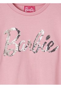 Rosa T-Shirt mit einem großen, geschwungenen "Barbie"-Schriftzug aus silbernen Pailletten. Der Stoff ist glatt und hat ein klassisches Rundhalsdesign.