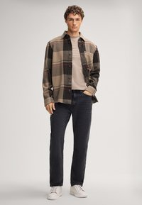 Chemise à carreaux en flanelle marron, beige et noir, superposée à un t-shirt beige, associée à un pantalon en denim foncé et des baskets blanches.