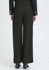 Pantaloni neri a gamba larga con trama, vita alta, due tasche sul retro e polsini con bottoni dorati. Tessuto liscio e strutturato.