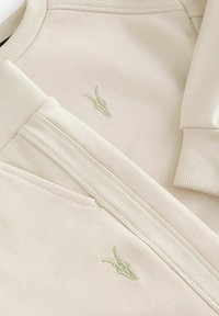 Beige sweatshirt med ribbede manchetter og bund, med et lys grønt broderet design. Blød tekstur og afslappet pasform.