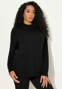 Zwarte gebreide trui met hoge hals, losse pasvorm en lange mouwen. Gladde textuur en ribbels aan de mouwen. Gecombineerd met zwarte legging.