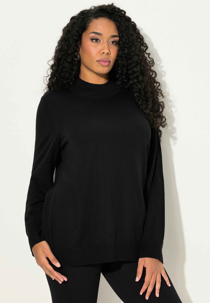 Zwarte gebreide trui met hoge hals, losse pasvorm en lange mouwen. Gladde textuur en ribbels aan de mouwen. Gecombineerd met zwarte legging.