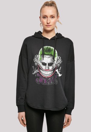 Svart hettegenser med grafikk av en Joker-karakter med grønt hår og et bredt smil. Snorhetter, lange ermer og avrundet nederkant.