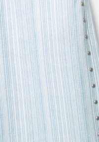 Tessuto di denim blu chiaro con strisce verticali. Presenta borchie in metallo argento lungo un lato, aggiungendo texture e dettagli al tessuto.