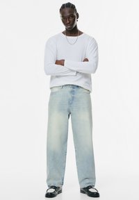 Jeans drepti de culoare albastru deschis, cu efect de decolorare, asortați cu o cămașă albă cu mânecă lungă. Sandale negre cu accent din plasă completează ținuta.