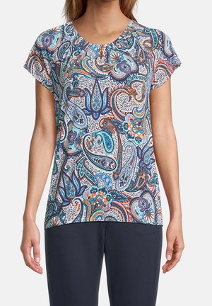 Femme portant une chemise à manches courtes avec un motif cachemire coloré en bleu, orange et turquoise, associée à un pantalon foncé.