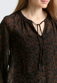 Bluse mit braunem Leopardenmuster aus leichtem, durchsichtigem Gewebe. Mit Knopfverschluss und Bindebändern am Ausschnitt. Müheloser Fall und Bewegung.