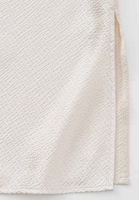 Textile de couleur crème avec une texture ondulée ; présente une fente sur le côté. La surface est légèrement froissée et lisse au toucher.