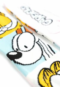 Calzini colorati con personaggi dei cartoni animati, principalmente in giallo, arancione e bianco. Il materiale è lavorato a maglia con una texture liscia e stampe audaci.