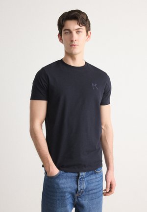 T-shirt en coton noir avec un col rond, coupe ajustée et petit logo brodé sur la poitrine gauche. Associé à un jean en denim bleu.