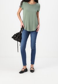 Grøn kortærmet top, blødt stof, bølget kant. Blå skinny jeans. Sort taske med blomsterprint. Sorte flade sko med nitter.