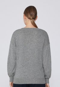 Grau gestrickter Pullover mit lockerer Passform, langen Ärmeln und gerippten Bündchen. Weiche Textur mit Rundhalsausschnitt und Nahtdetails auf der Rückseite.