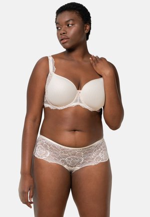 Soutien-gorge en dentelle beige avec un design côtelé et des accents floraux, assorti à un shorty en dentelle présentant un motif floral le long des bords.
