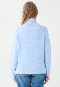 Helles blaues, strukturiertes Strickoberteil mit hohem Kragen und gerippten Bündchen. Besitzt einen leicht lockeren Schnitt und einen geraden Saum hinten.