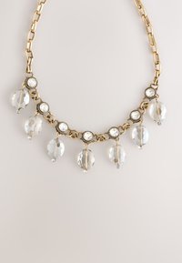 Gold chain necklace with clear, faceted beads and round, sparkling accents, featuring dangling crystal-like ornaments.