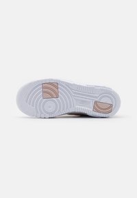 Valkoiset tennarit, joiden pohjassa on teksturoitu kumi, pyöreitä kuvioita ja vaaleanruskea korostuslohko. Mukana Nike-logot ja kaareva muotoilu.