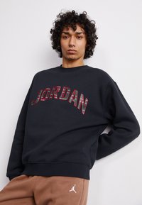 Felpa nera con la scritta "JORDAN" in lettere a quadri rosse e verdi. Tessuto morbido, colletto a girocollo e vestibilità comoda.