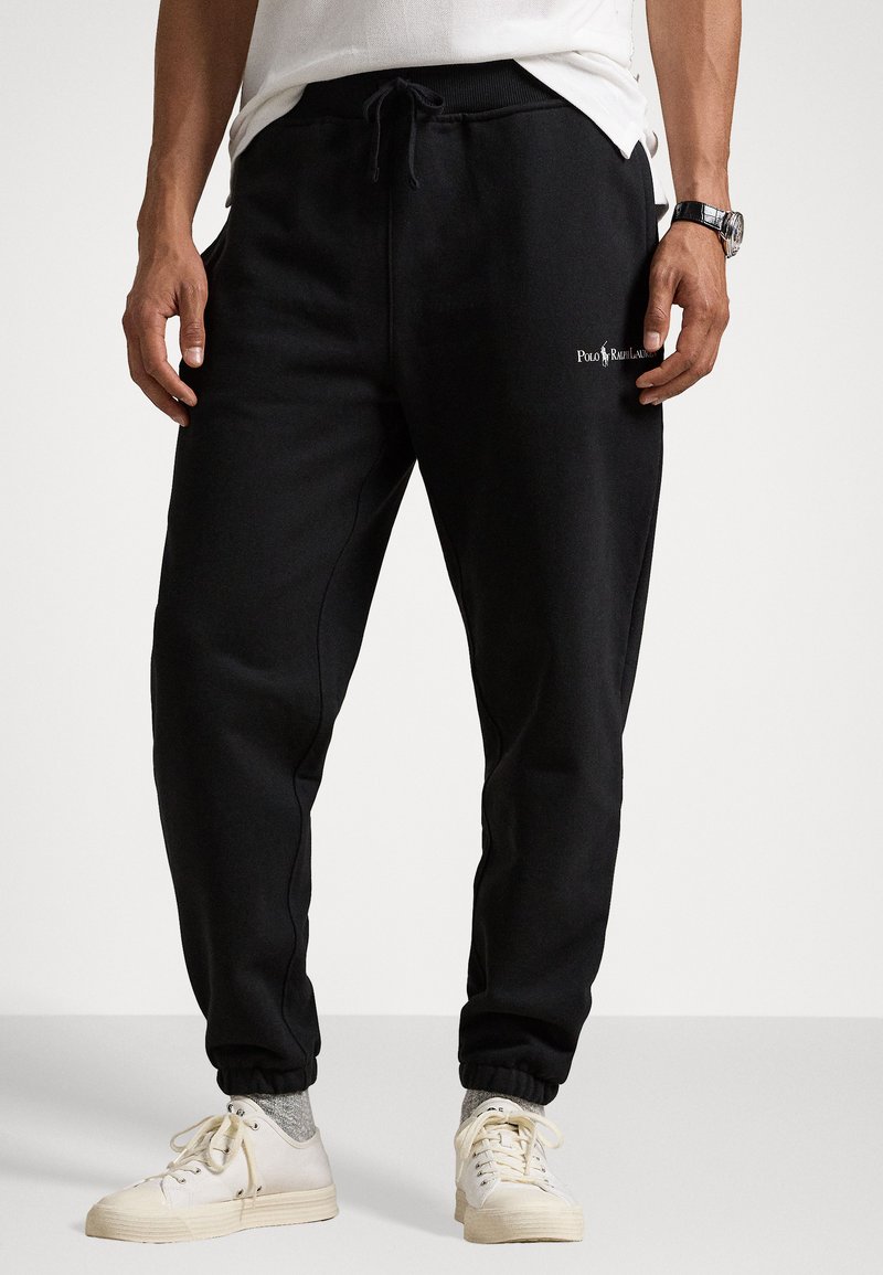 Schwarze Sweatpants aus weichem Material, mit elastischem Bund und verstellbarem Kordelzug, gerippten Bündchen und einem Logo an der linken Oberschenkel.