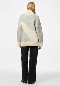 Üks suur mõõtmed kudum, helehall koos kreemjate aktsentidega, millel on kõrge krae ja ribadega äär, koos mustade laiade pükstega.