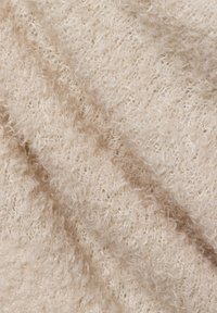 Weicher, plüschiger Stoff in hellem Beige mit einer strukturierten, leicht lockigen Oberfläche, die unregelmäßige Muster und ein gemütliches Aussehen aufweist.