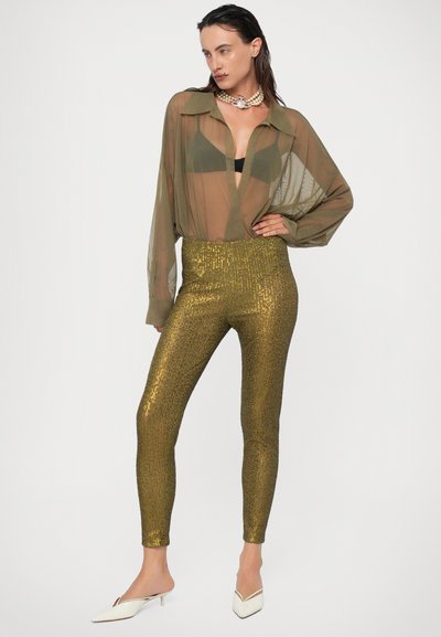 Priesvitná olivovo zelená košeľa s golierom, čierna podprsenka pod ňou; legíny so zlatými flitrami; biele nízke podpätky; perlový náhrdelník.