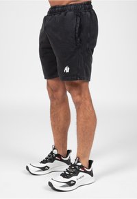 Zwarte katoenen shorts met een elastische tailleband, zijzakken en een witte gorilla logo. G gedragen in combinatie met witte en zwarte hardloopschoenen.