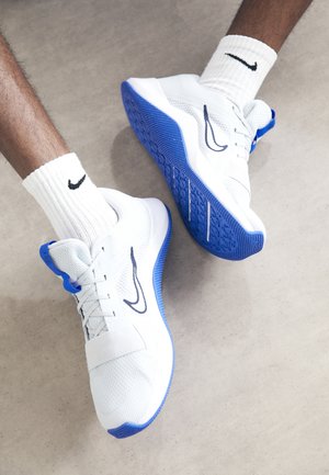 Baskets Nike blanches et bleues portées avec des chaussettes Nike blanches sur un sol gris clair.