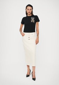 Camiseta negra con un gráfico de oso y el logotipo de "Moschino", combinada con una falda midi blanca de cintura alta con botones y una silueta recta.