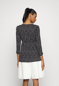 Top preto com bolinhas brancas, com mangas três quartos e cintura franzida, combinado com uma saia branca texturizada.