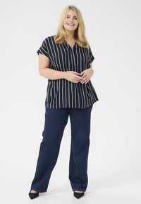 Blouse bleu marine à boutonnage, avec des rayures beiges, des manches courtes et une coupe décontractée, associée à un pantalon droit bleu foncé et des chaussures à bouts pointus noires.