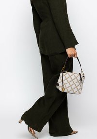 Person wearing dark green suit and beige heeled sandals, holding a white and beige patterned handbag with brown straps.