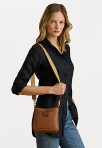 Καφετί δερμάτινος τσάντα crossbody με υφή, χρυσές μεταλλικές λεπτομέρειες και μονόγραμμα στο μπροστινό μέρος. Ρυθμιζόμενος καμβάς σε μπεζ χρώμα με λεπτομέρεια λογότυπου.