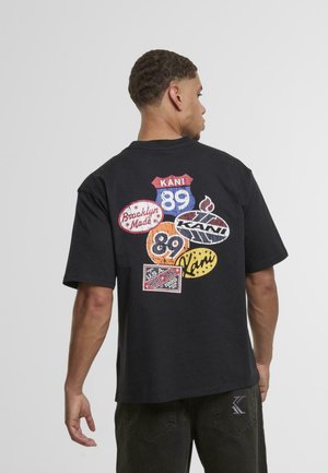 Black cotton t-shirt featuring a colorful graphic design on the back with various labels and logos, showcasing different shapes and colors.