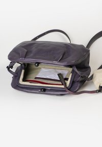 Lila Leder-Umhängetasche mit einem Reißverschlussverschluss. Das Innere verfügt über ein gestreiftes Stofffutter und eine kleine rote Tasche. Verstellbarer Tragegurt.