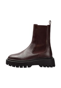 Botas Chelsea de cuero marrón con paneles elásticos laterales, puntera redonda y suela gruesa y chunky negra con surcos profundos para mayor tracción.