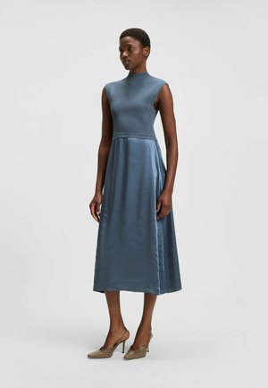 Un vestito senza maniche di lunghezza midi in un morbido tessuto blu tenue, con un corpetto aderente e una gonna svasata, abbinato a scarpe con tacco neutre.