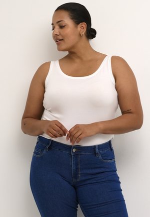 Top sin mangas de algodón blanco con escote redondeado, combinado con jeans de mezclilla azul oscuro que presentan costuras estándar y cierre frontal con botones.