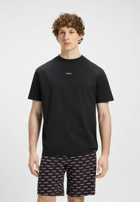 T-shirt noir en coton à manches courtes avec un col rond et un petit logo rouge "HUGO" sur la poitrine, associé à un short noir à motifs arborant le même logo.