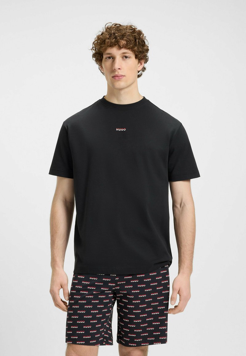 T-shirt noir en coton à manches courtes avec un col rond et un petit logo rouge "HUGO" sur la poitrine, associé à un short noir à motifs arborant le même logo.