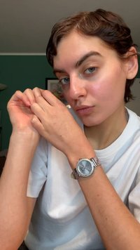 Sølvur med rund, blå urskive og krystalbesætninger på en tekstureret rem, båret på et lyst hudfarvet håndled. Hvid t-shirt i baggrunden.