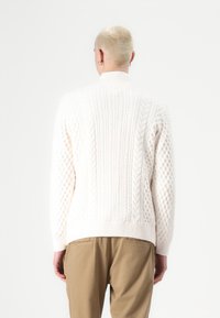 Gebreide trui in off-white met verschillende textuurpatronen, waaronder kabel- en bobble-ontwerpen, en een geribde kraag en zoom.