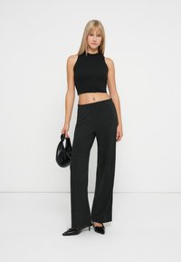 Sort udenærmet crop top parret med mørkegrå, brede bukser, iført sorte hæle og holder en sort håndtaske. Glat stoftekstur.
