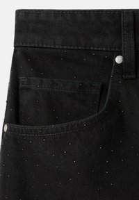 Jeans de mezclilla negra con un bolsillo frontal, adornados con pequeños puntos plateados dispersos por toda la superficie, con costuras en contraste.
