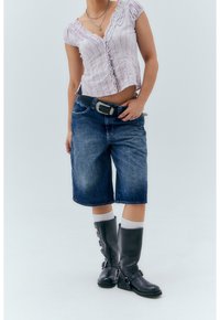 Ljuslila topp med korta ärmar och vågiga kanter, tillsammans med blå denim Bermudashorts och knähöga svarta stövlar med sidospännen.