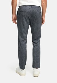 Grå mønstrede bukser lavet af struktureret stof, med en skræddersyet pasform, to baglommer, og båret med hvide sneakers.